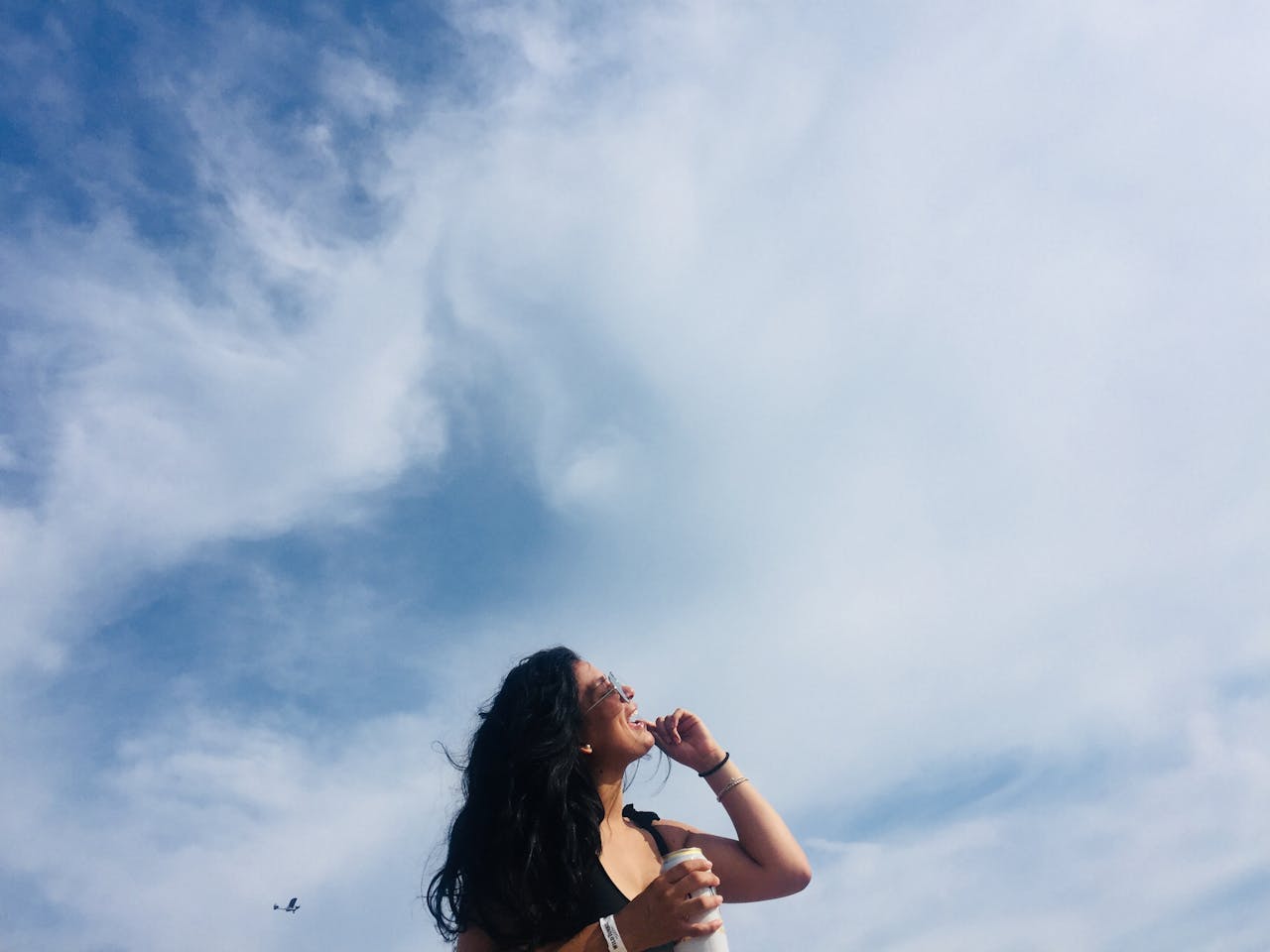 Smiling woman enjoys a sunny day at Atlantic City beach, holding a drink with a clear blue sky above.