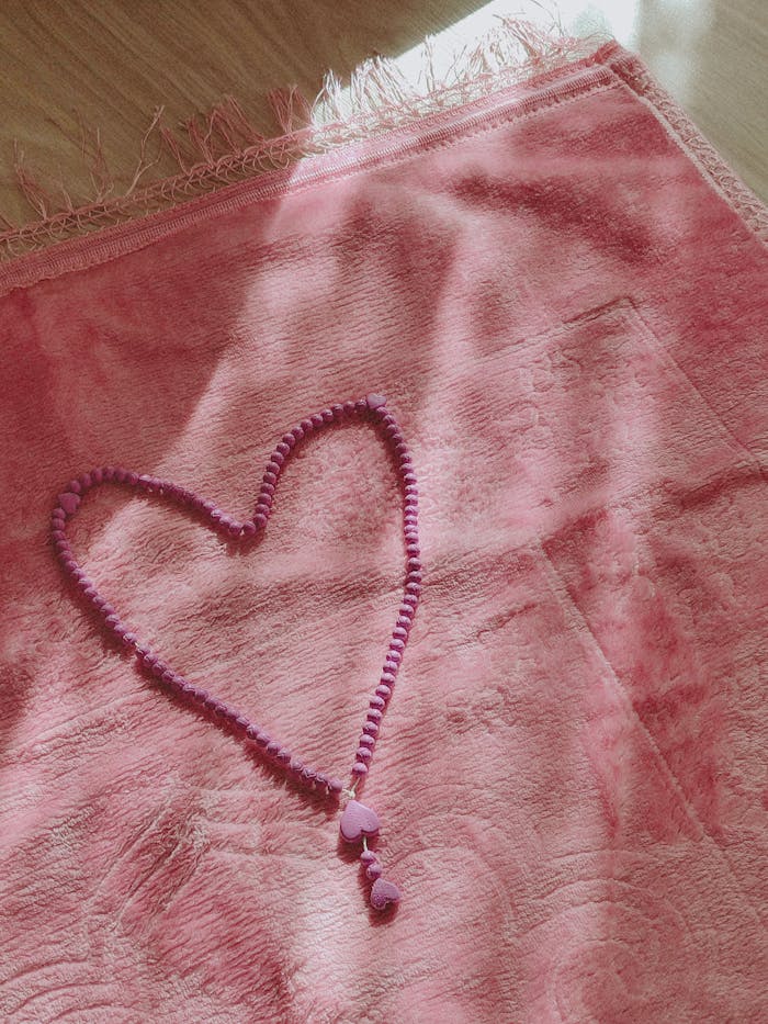 Heart-shaped pink prayer beads on textured pink cloth in soft light.